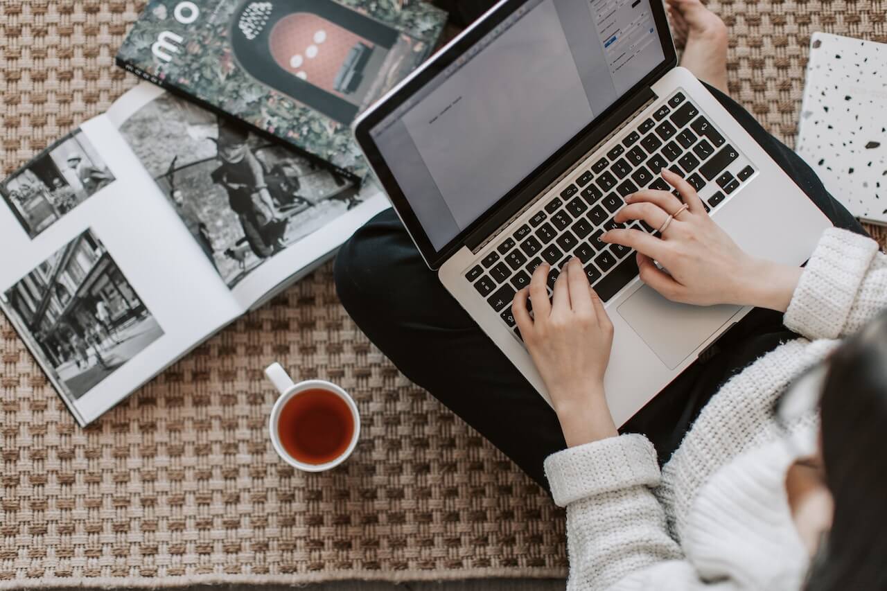 woman typing on laptop with books in background 